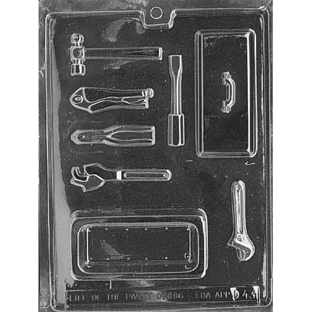 Clear plastic chocolate mold photographed on a black background with cavities shaped like a toolbox base and lid with handle, plus small tool shapes including a hammer, pliers, adjustable wrench, and screwdriver.