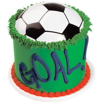 Vibrant soccer ball cake with 'GOAL!' lettering, featuring a black and white soccer ball half-embedded in green icing with grass details and a border of red and white. Ideal for soccer fans and sports-themed parties.