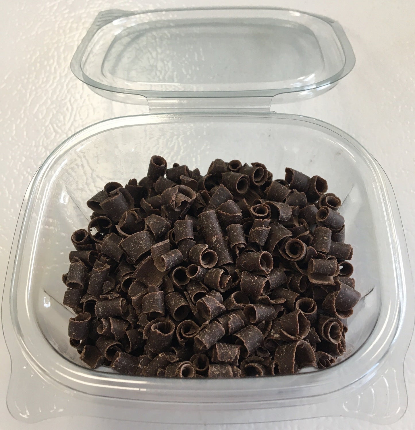 Clear plastic container of dark chocolate curls with lid open, ready for use as dessert toppings.
