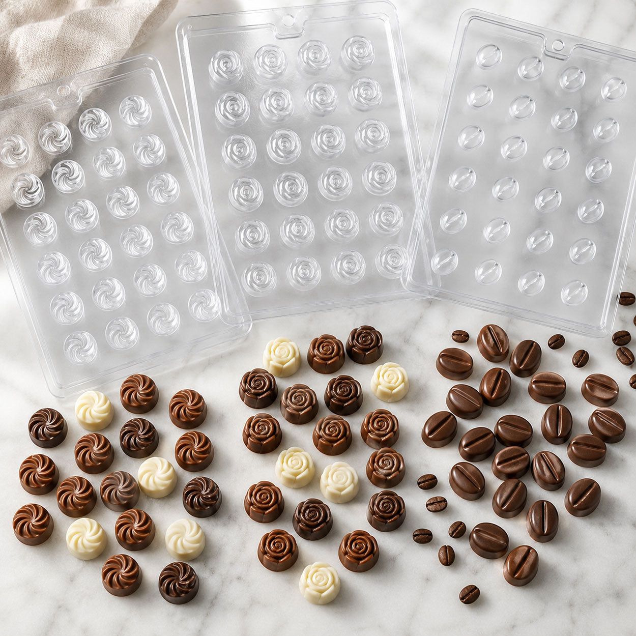 Truffle and bon bon chocolate molds with swirl, rose, and coffee bean designs, displayed with finished milk, dark, and white chocolates.
