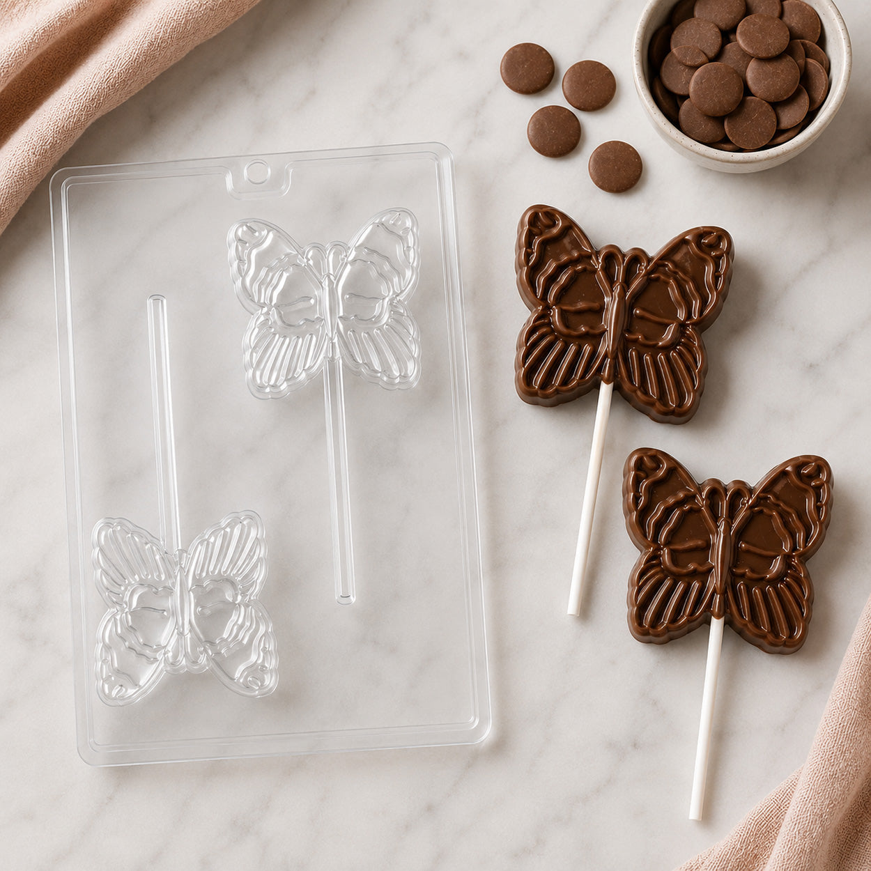 Butterfly chocolate lollipop mold with finished milk chocolate butterfly pops, chocolate candy melts, and candy-making supplies on a marble surface.