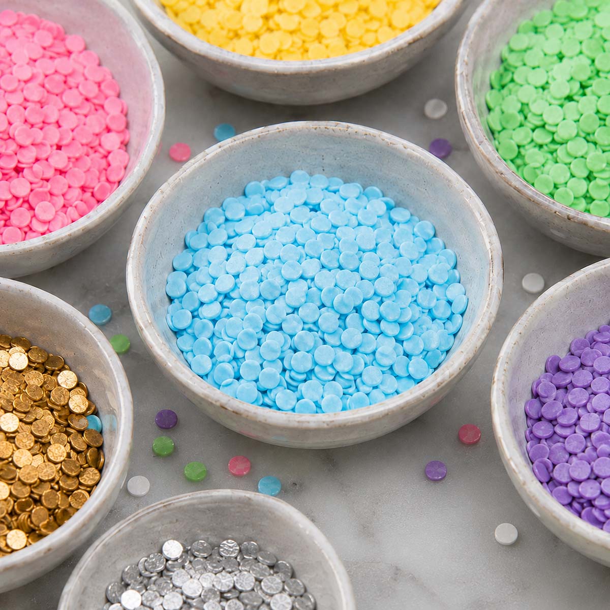 Bowls of colorful confetti sprinkles in pastel, gold, silver, and rainbow colors for cake and cupcake decorating.
