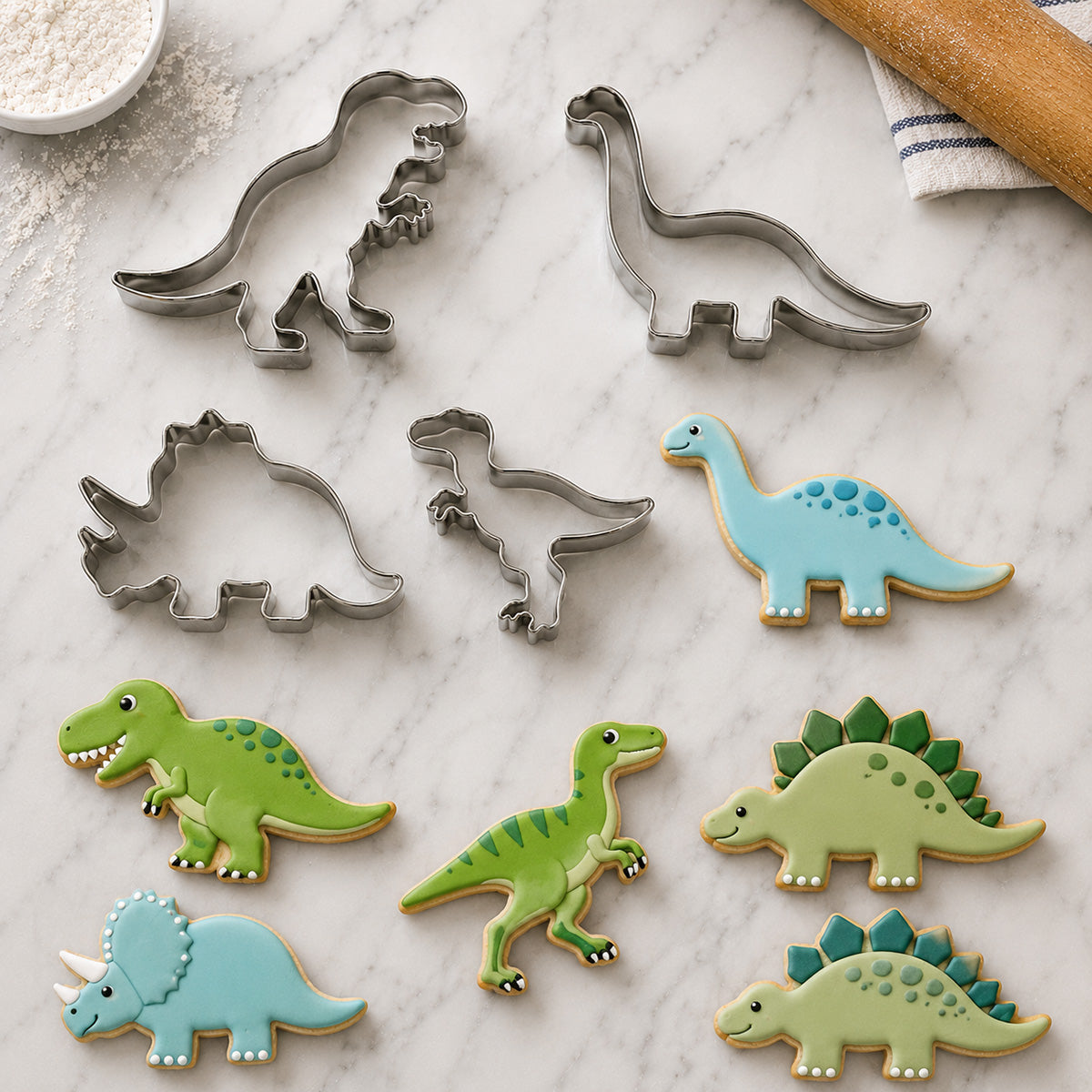 Dinosaur-themed cookie cutters and decorated cookies shaped like T-Rex, Brontosaurus, Triceratops, Stegosaurus, and Velociraptor on a marble baking surface.
