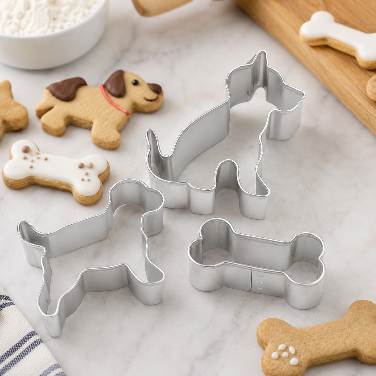 Dog-themed cookie cutters and decorated dog bone cookies displayed on a marble surface, featuring dog-shaped and bone-shaped baking cutters.