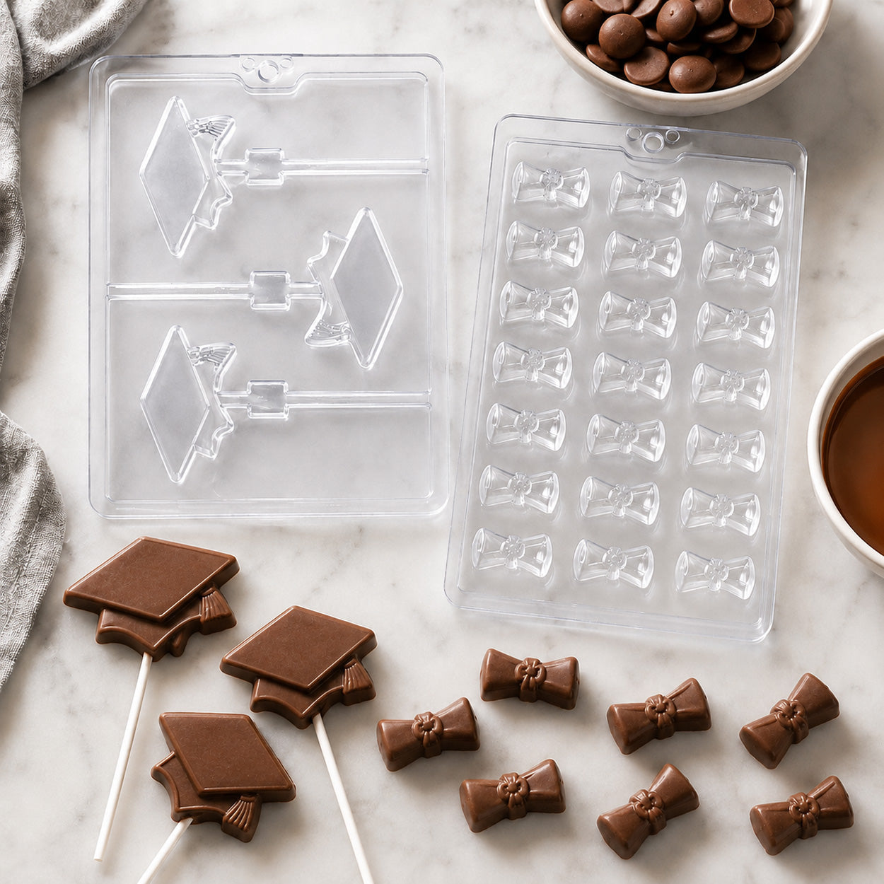 Graduation chocolate candy molds featuring graduation cap lollipops and diploma scroll candies with finished milk chocolate treats, candy melts, and melted chocolate.