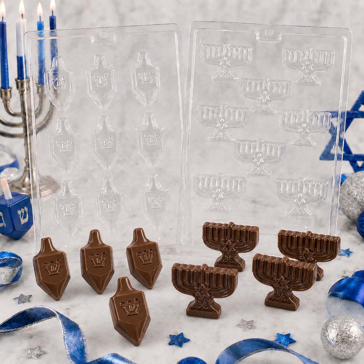 Hanukkah chocolate molds featuring dreidels and menorahs with finished milk chocolate candies, styled with candles, ribbon, and festive décor.