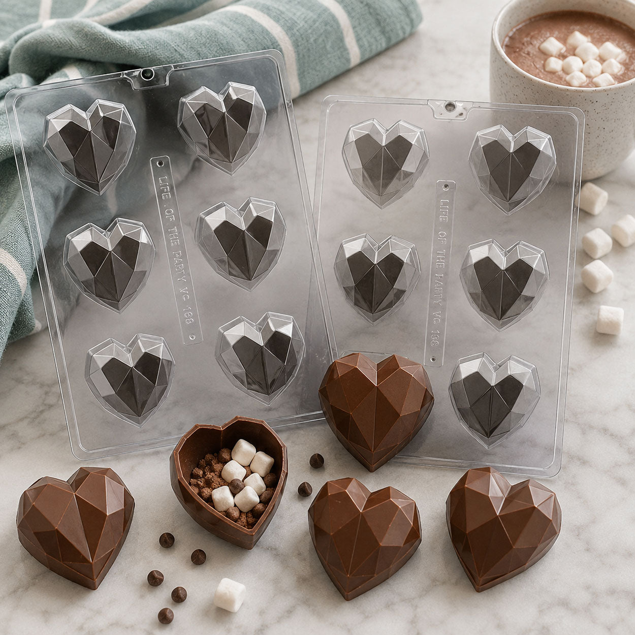 Geometric heart hot chocolate bomb molds with finished chocolate cocoa bombs, marshmallows, and hot cocoa for Valentine's Day candy making.