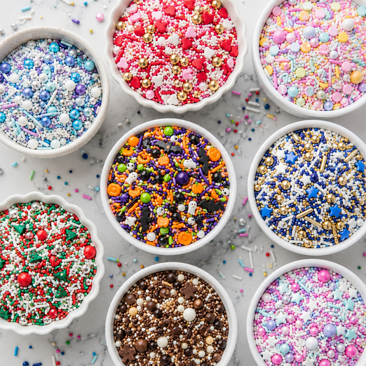 Bowls of colorful themed sprinkles blends and mixes with candy pearls, stars, hearts, pumpkins, and holiday shapes on marble.
