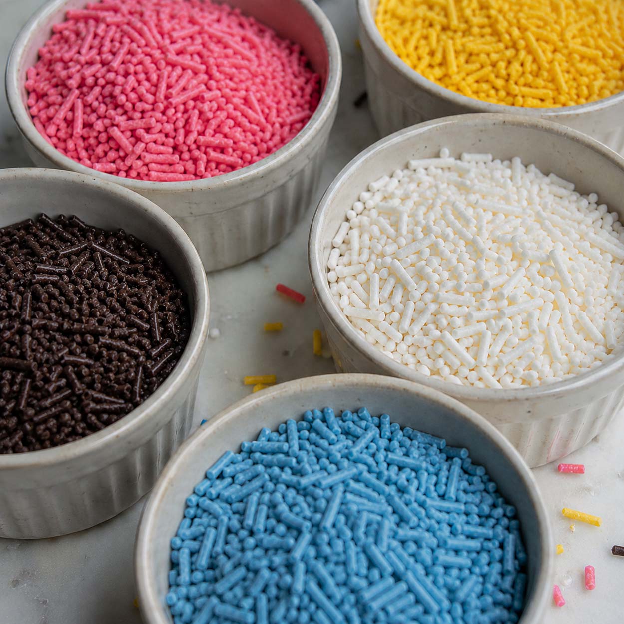 Bowls of pink, yellow, white, blue, and chocolate jimmies sprinkles for cake and cupcake decorating.