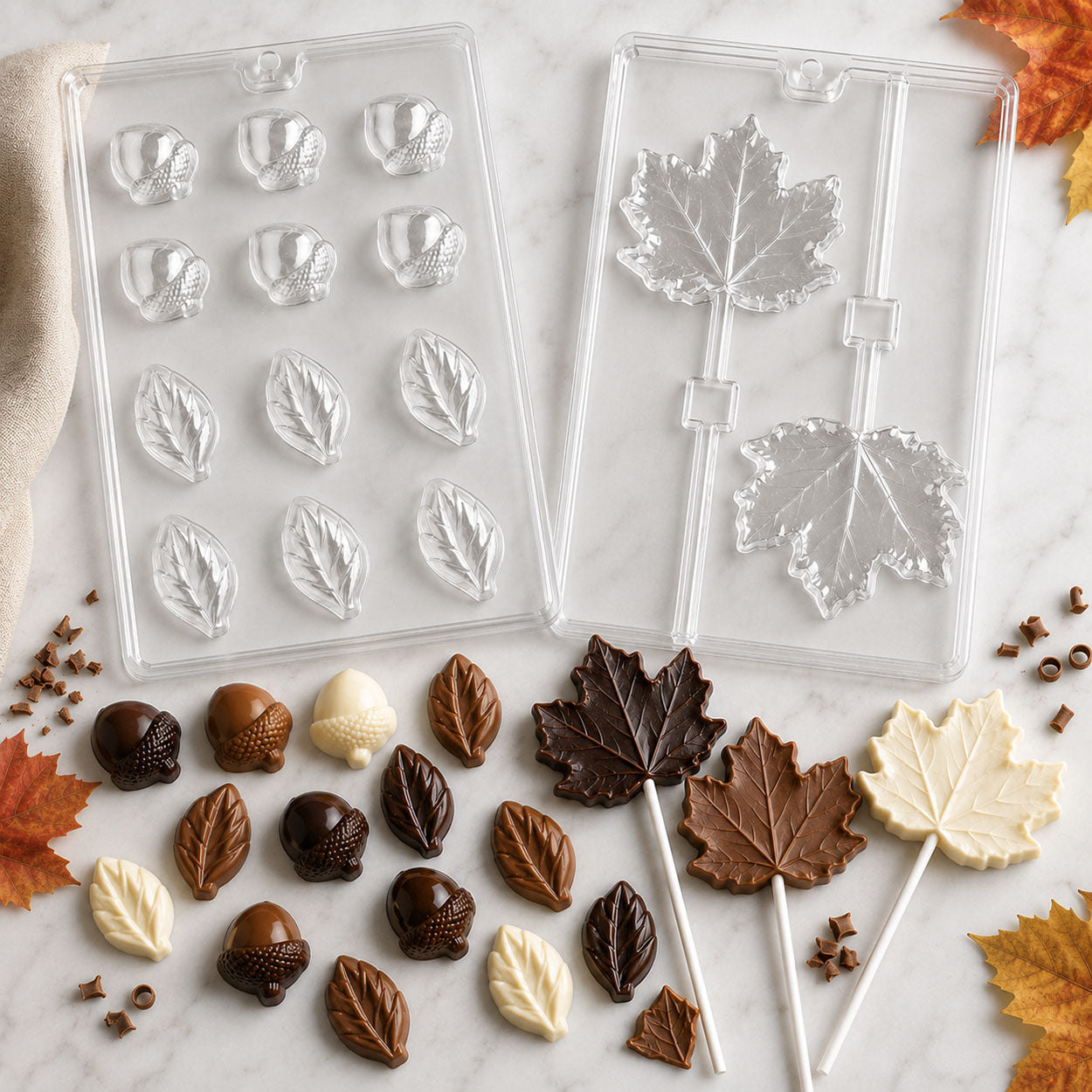 Autumn chocolate molds with acorns, leaves, and maple leaf lollipops, featuring finished milk, dark, and white chocolate fall-themed candies.