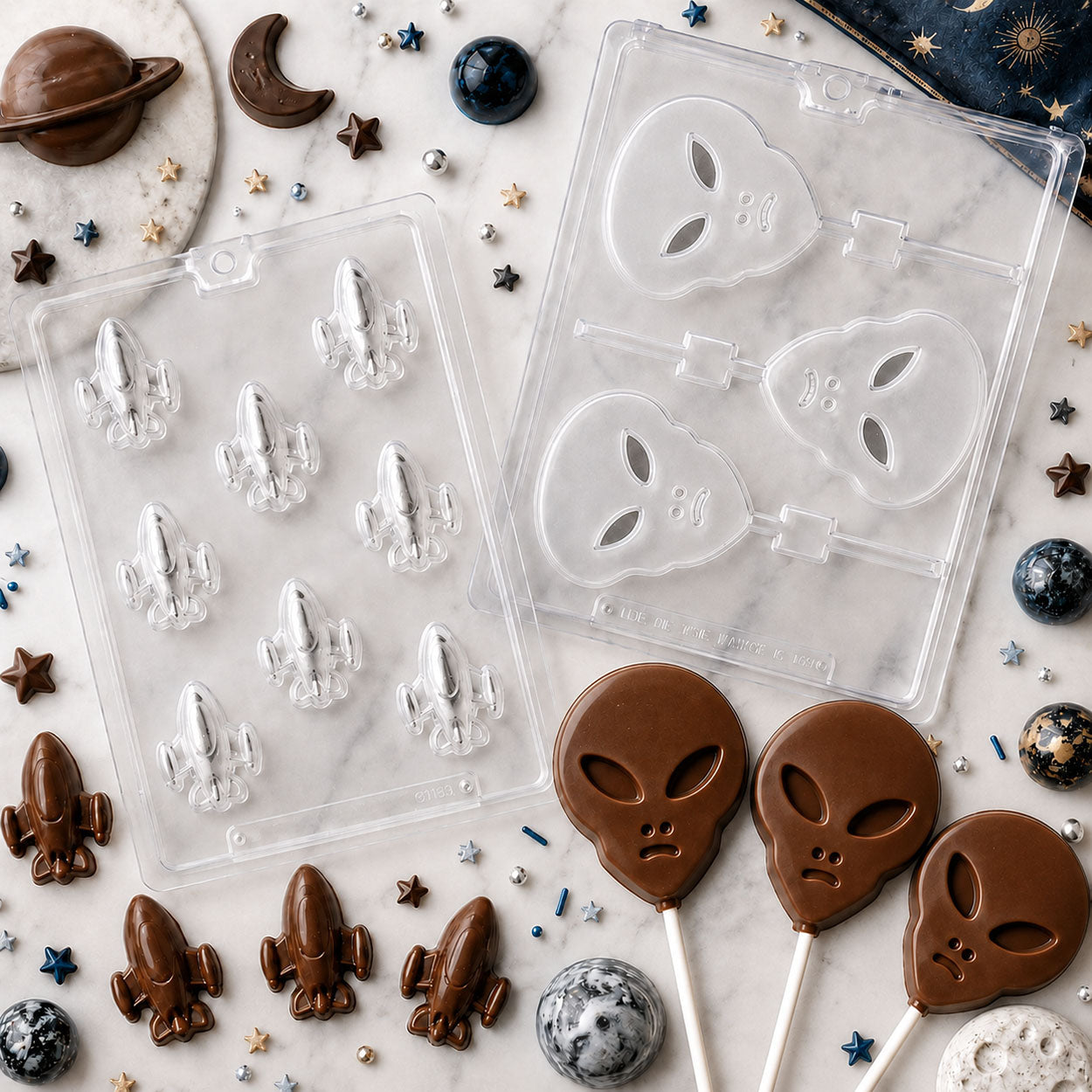 Outer space chocolate molds featuring rocket ships and alien lollipops with finished milk chocolate candies, styled with planets, stars, and moon décor.