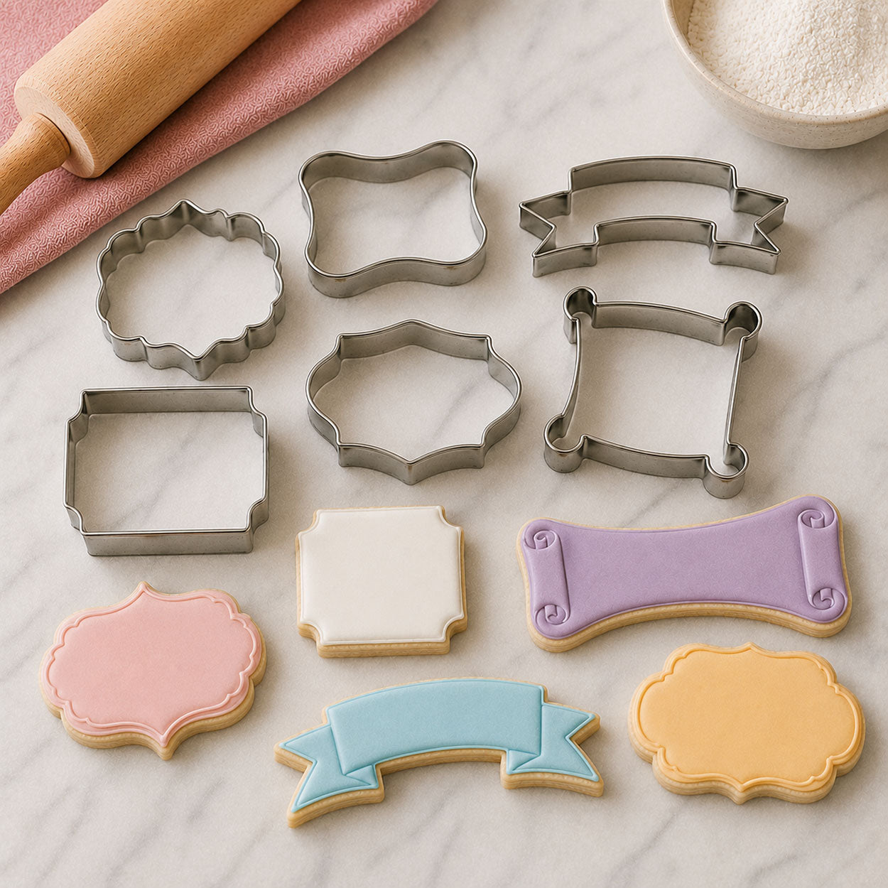 Plaque, frame, banner, and scroll cookie cutters displayed with pastel decorated cookies on a marble baking surface.