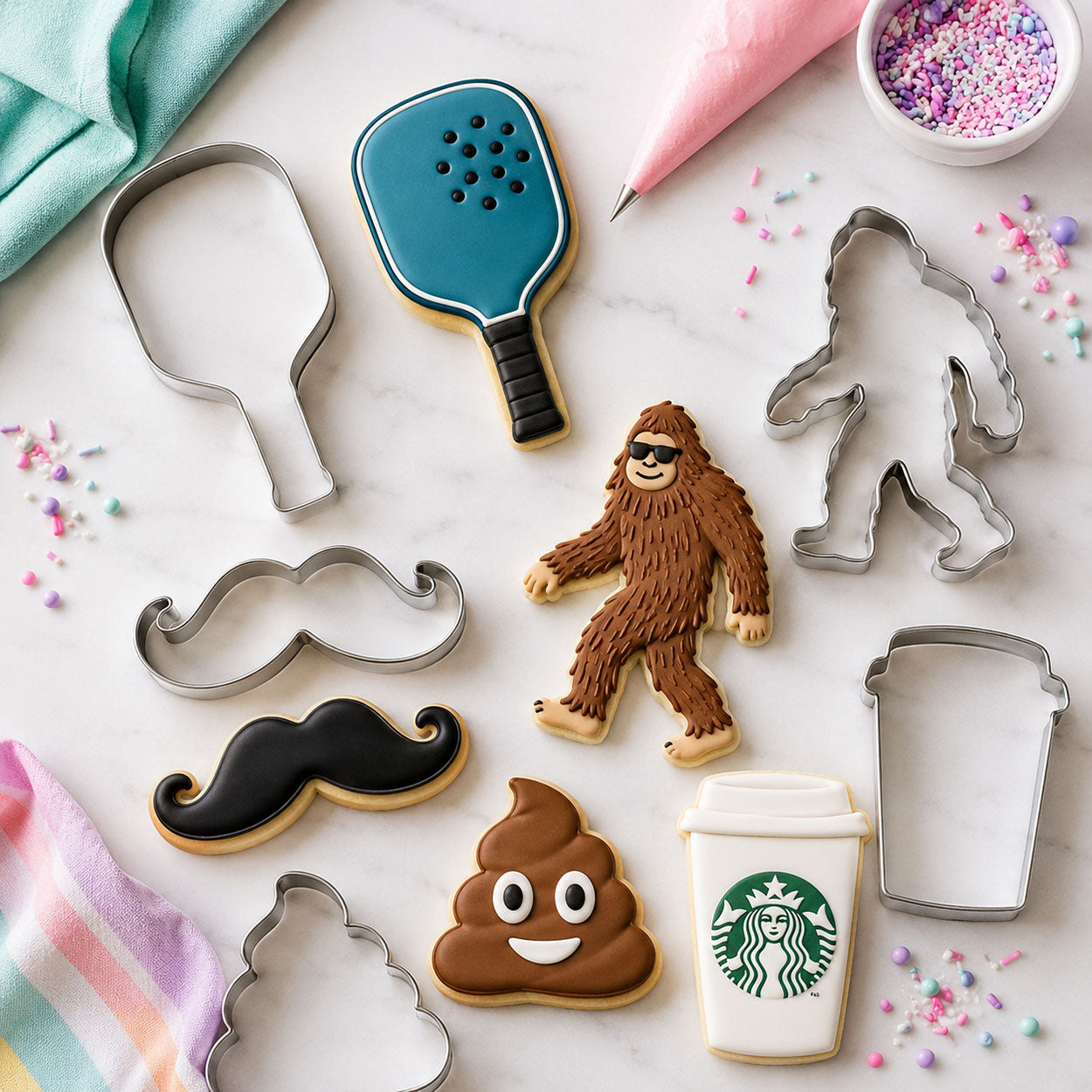 Novelty cookie cutters and decorated cookies shaped like a pickleball paddle, Bigfoot, mustache, poop emoji, and coffee cup.