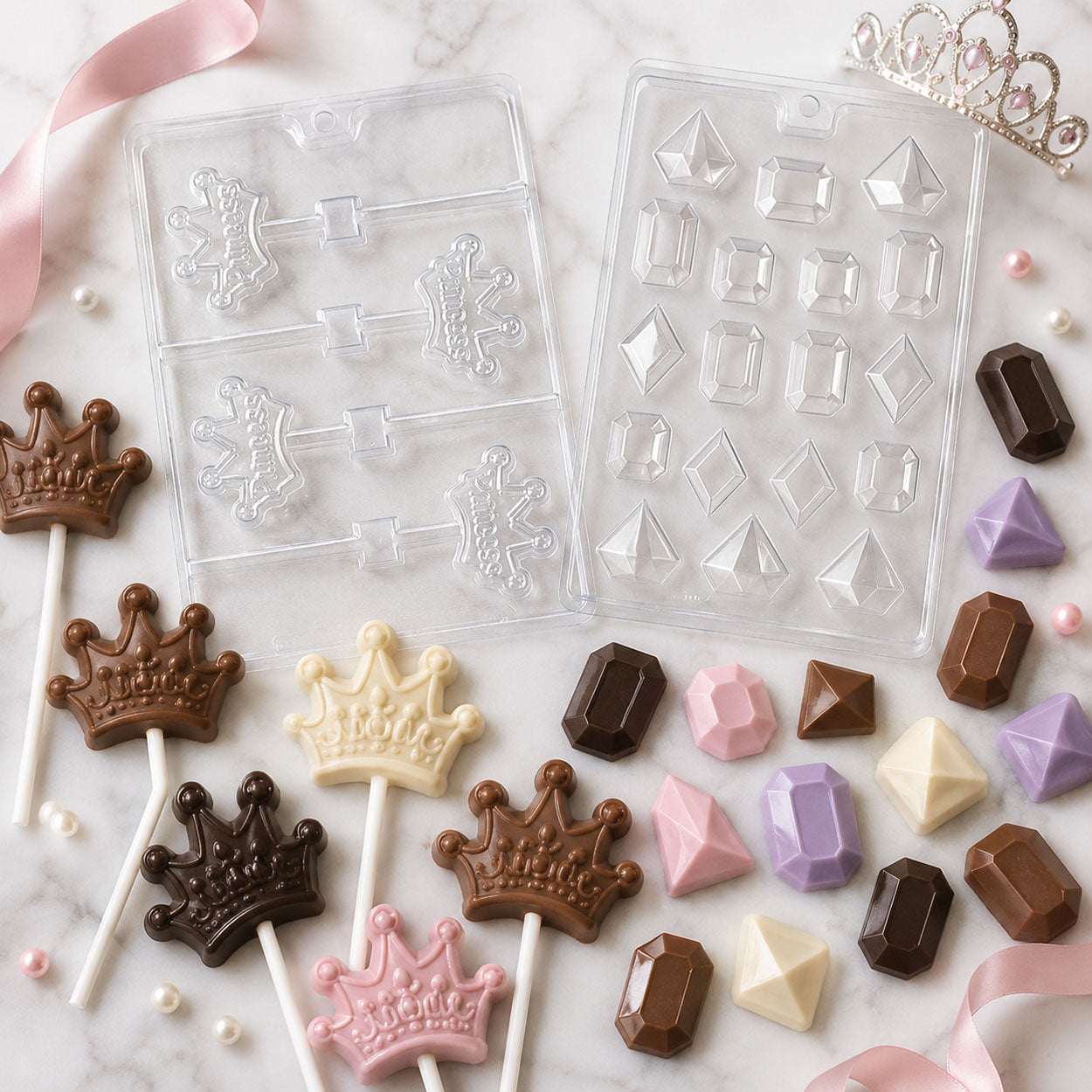 Princess chocolate molds with crown lollipops and gemstone candies in milk, dark, white and pastel chocolate on a marble surface.