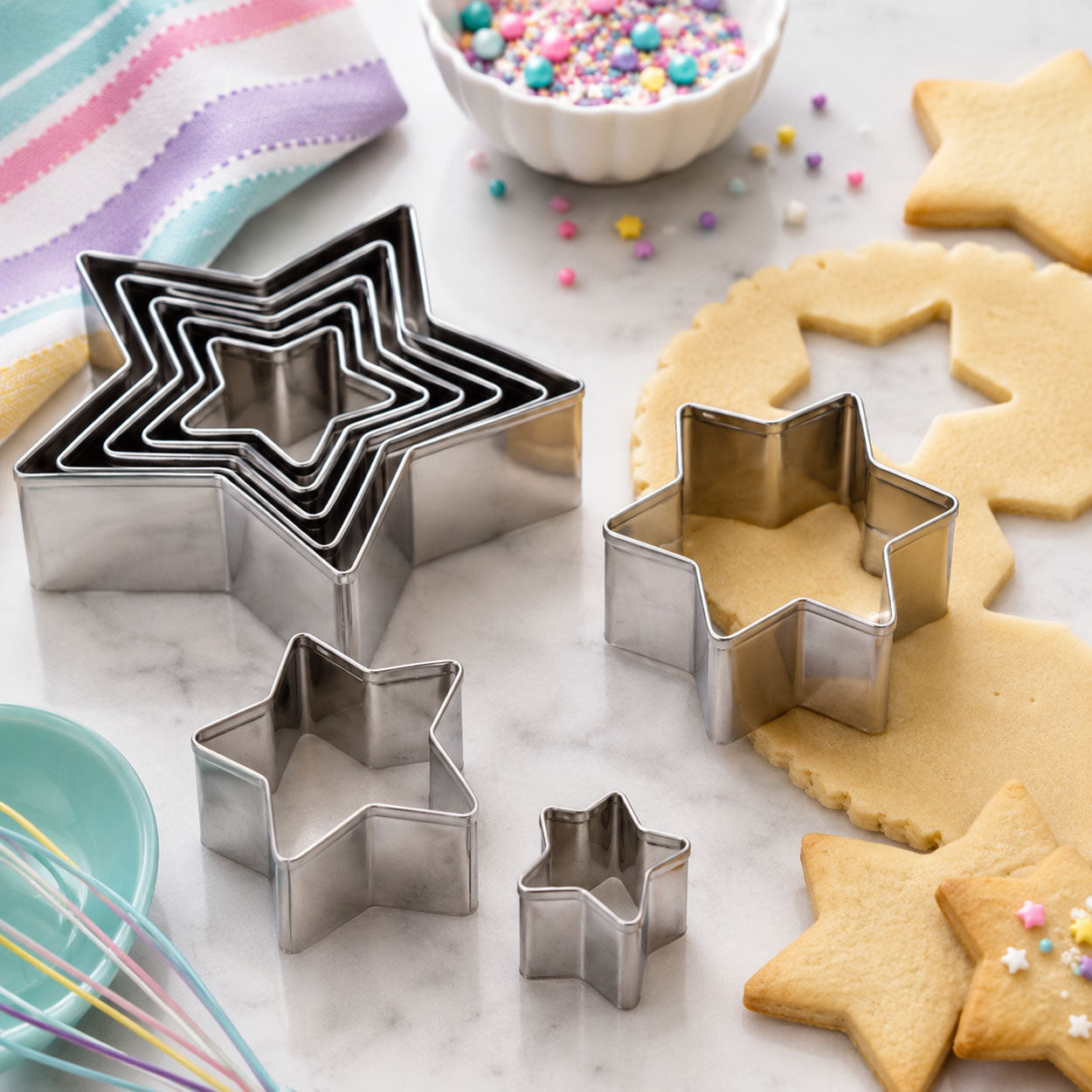 Star-shaped cookie cutters in assorted sizes displayed with cut dough, baked star cookies, colorful sprinkles, and baking tools.