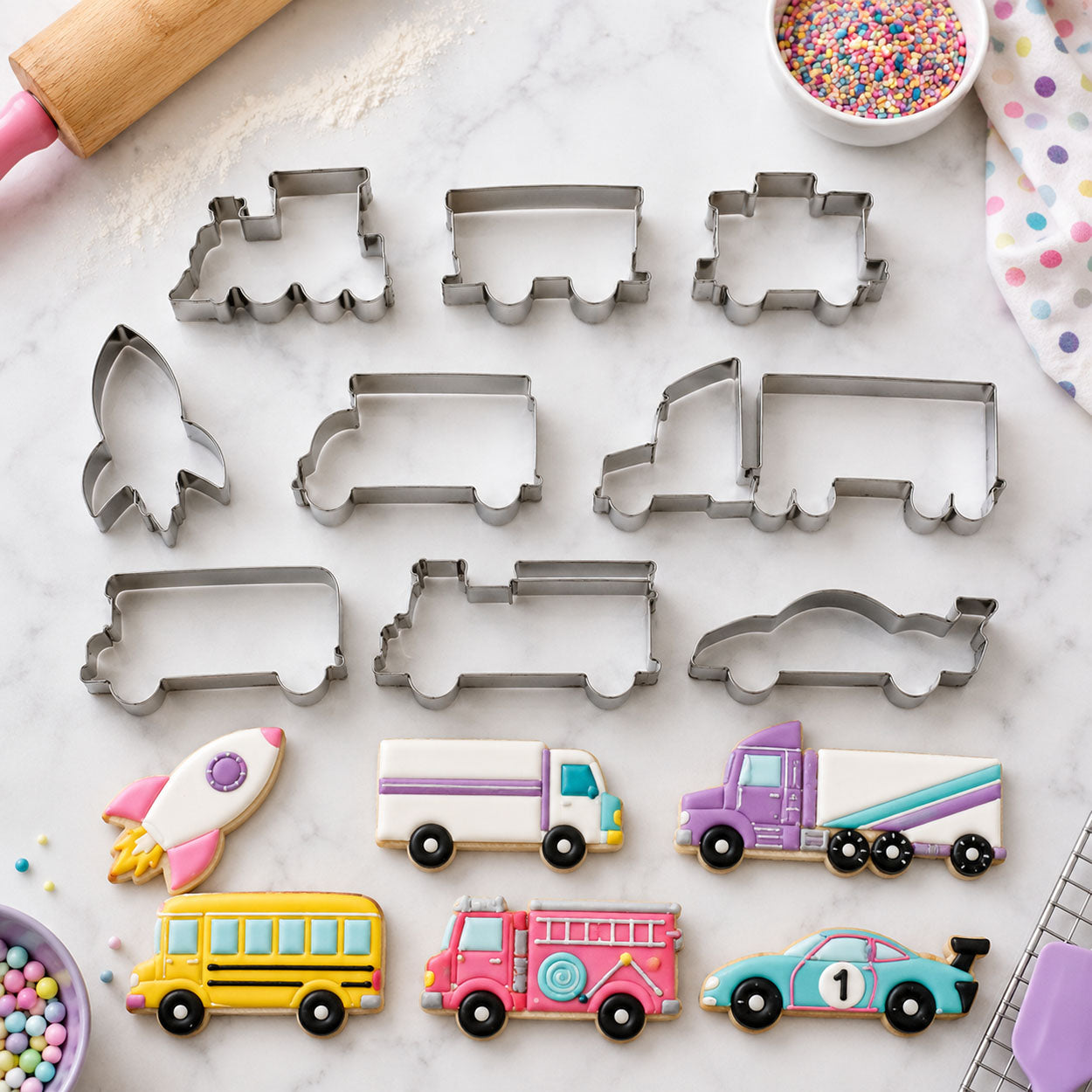 Vehicle cookie cutters and decorated truck, bus, rocket and race car sugar cookies on a marble baking surface