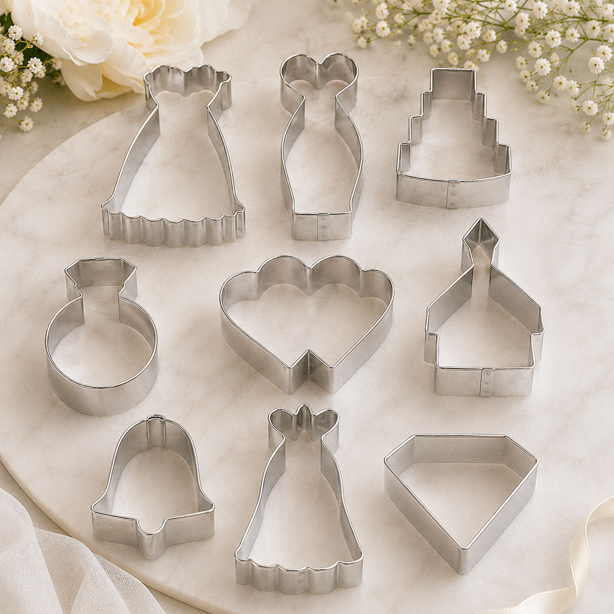 Wedding cookie cutters in dress, cake, ring, hearts, church, bell and diamond shapes on a marble surface with white flowers