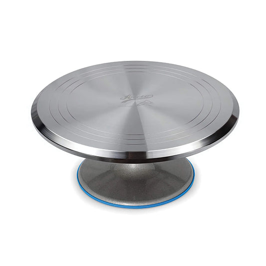 Ateco 12-inch aluminum cake decorating turntable with a brushed silver round top, concentric guide rings, raised pedestal base, and blue non-slip silicone edge.