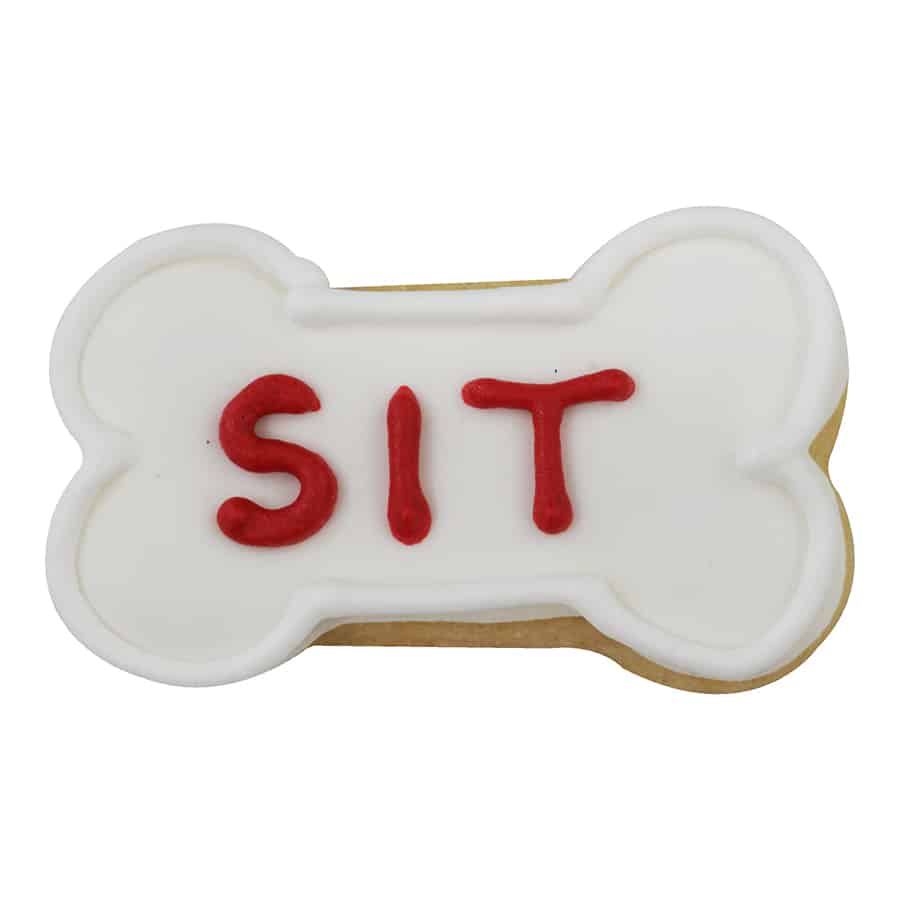 Dog bone-shaped cookie decorated with white icing and the word 'SIT' in red, made with the 2-inch cookie cutter.