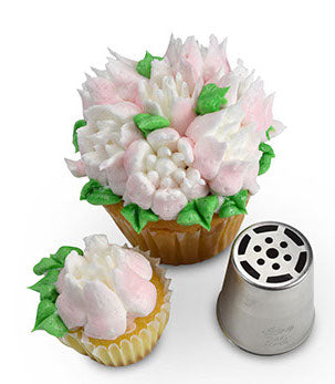 Cupcake topped with vibrant pink frosting flowers and green leaves, created using Russian Piping Tip #246. The metal piping tip is placed next to the cupcake, demonstrating its detailed design.