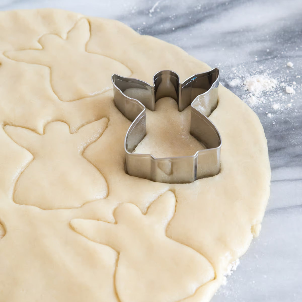 Angel cookie cutter pressing into rolled-out dough with multiple angel shapes cut out.