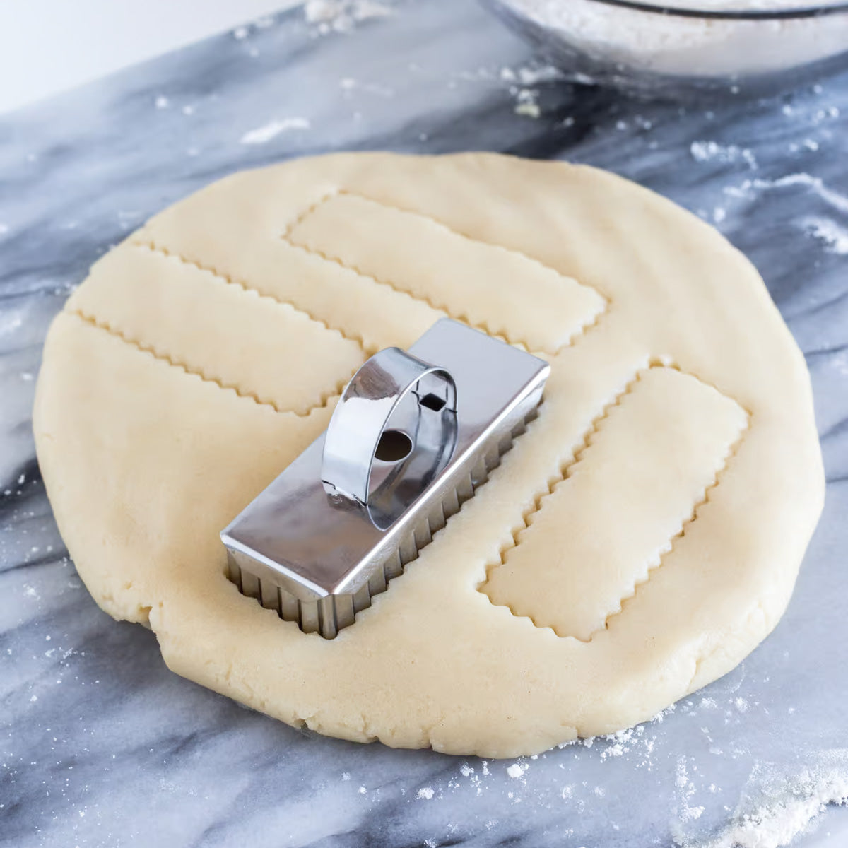 Shortbread cutter in use, cutting uniform cookie shapes from dough on a marble surface.