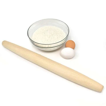 Wooden French rolling pin placed beside a bowl of flour and two eggs, one brown and one white, on a white background.