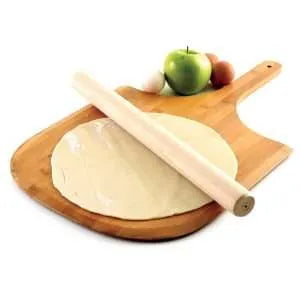 Wooden rolling pin placed on a round pizza dough, which is on a wooden cutting board with an apple and eggs in the background.