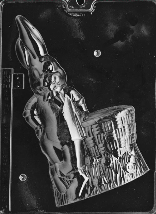 Clear plastic chocolate mold showing the front half of a tall bunny leaning on a woven basket, with defined face details, long ears, and textured grass base.