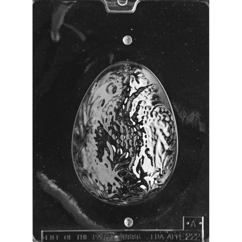 Close-up of top half of a two-piece 3D decorated Easter egg chocolate mold, showing an oval egg cavity with an ornate raised scroll and floral relief pattern.