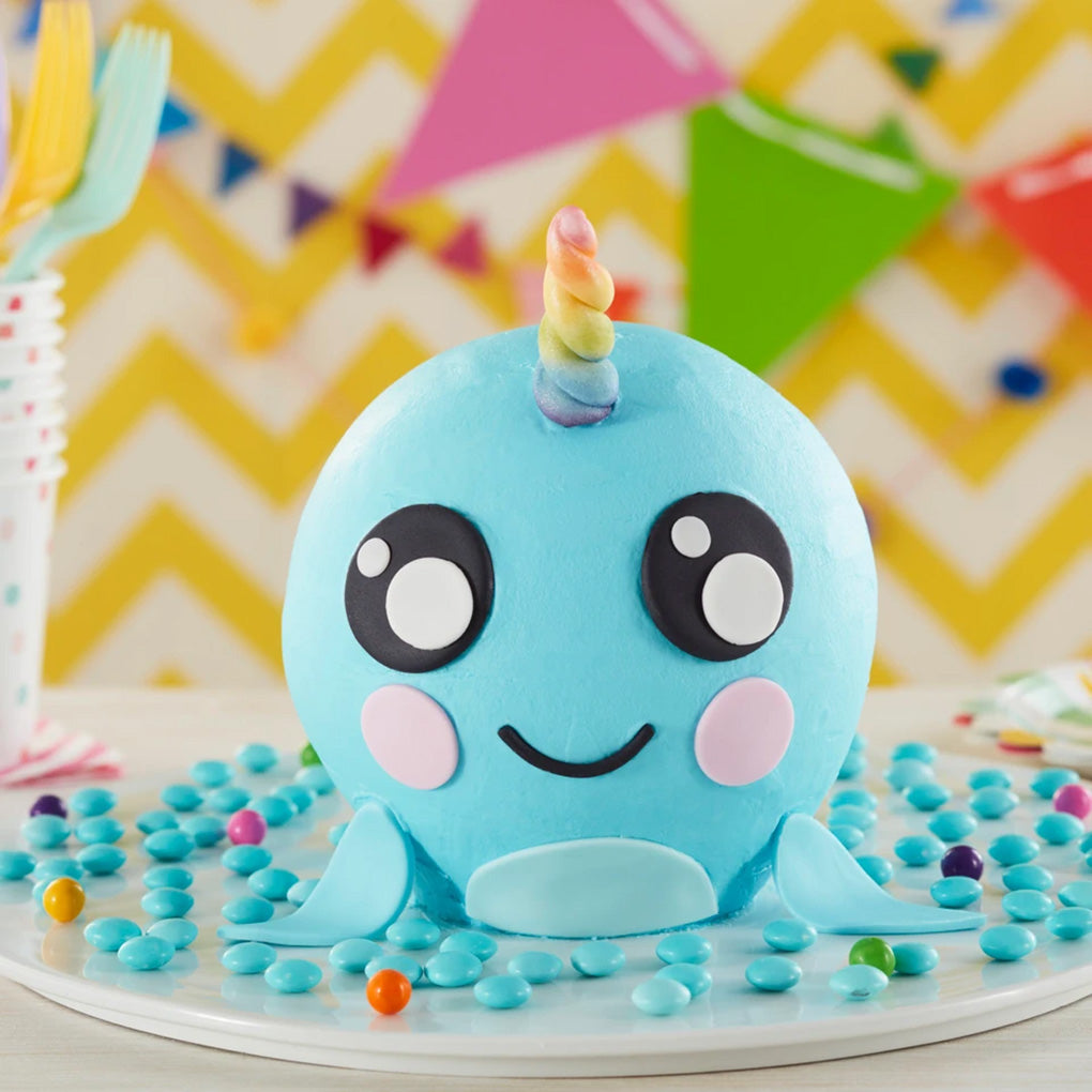 Blue baby narwhal ball cake with a rainbow horn, fondant face, and flippers, made with the Wilton 3D Ball Cake Pan Set