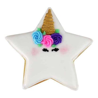 A star-shaped sugar cookie decorated as a unicorn, featuring white icing, colorful floral accents, and a golden horn.