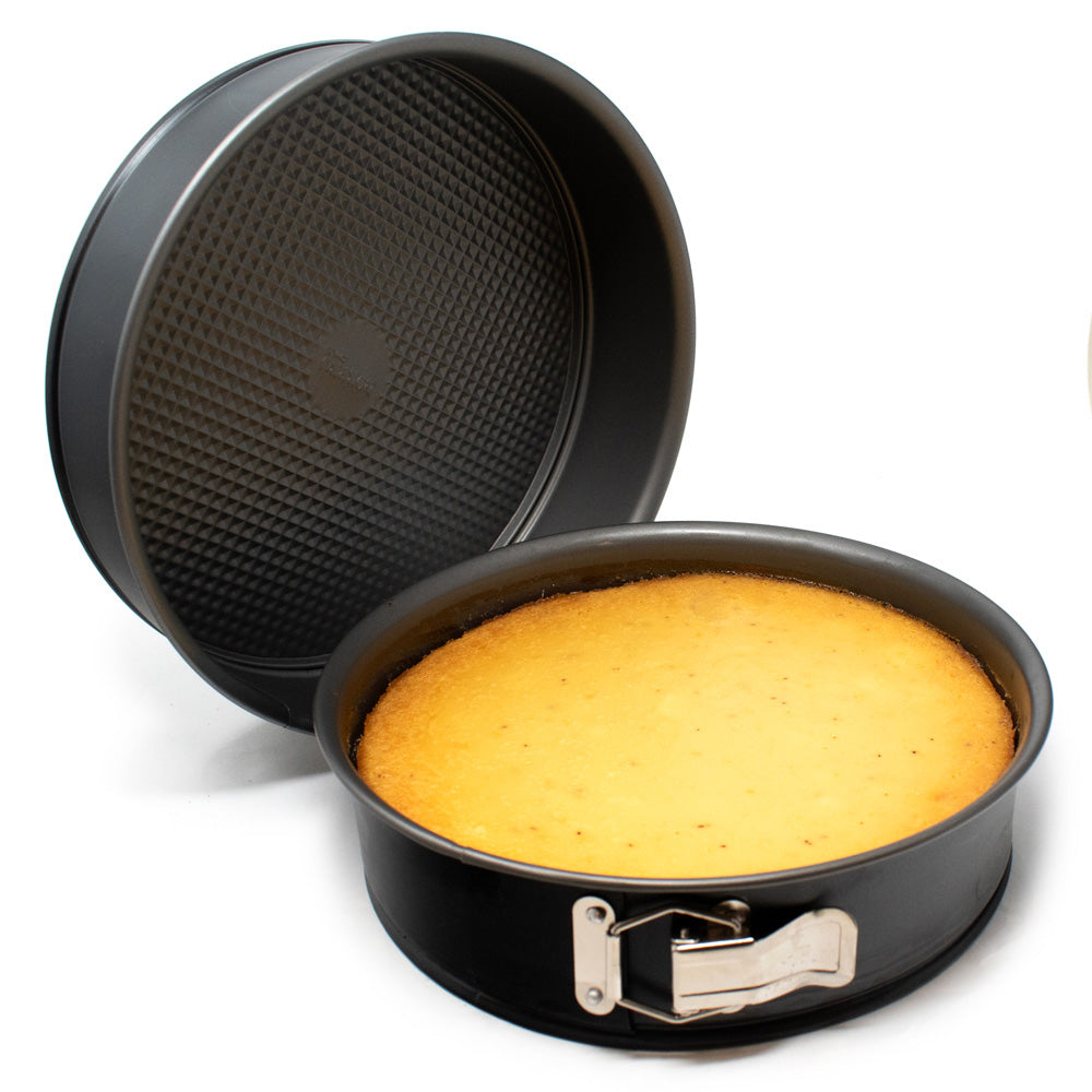 Black nonstick springform pan holding a golden cheesecake beside a second pan showing the textured removable base and deep round sides.