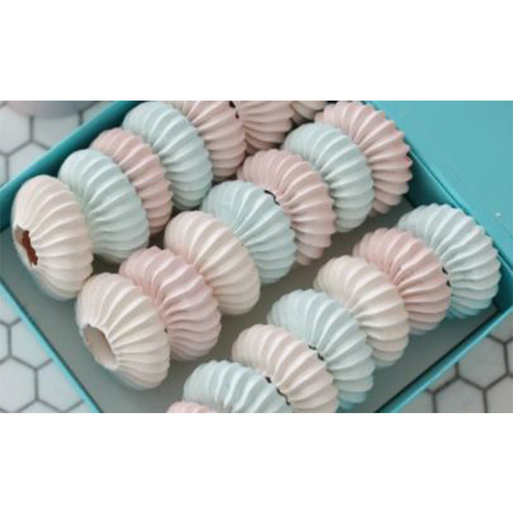 Box filled with pastel pink and light blue ruffled ring cookies piped with a sultan tip, arranged in rows inside a teal box.
