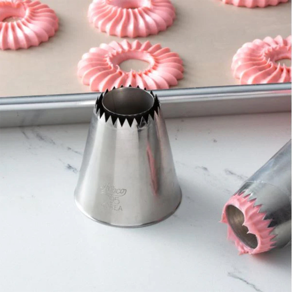 795 Sultan flat cone piping tip on a countertop near piped pink ruffled ring cookies on a baking sheet, with another metal tip in the foreground.