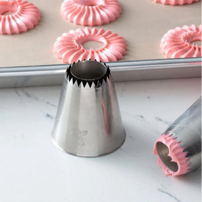 795 Sultan flat cone piping tip on a countertop near piped pink ruffled ring cookies on a baking sheet, with another metal tip in the foreground.