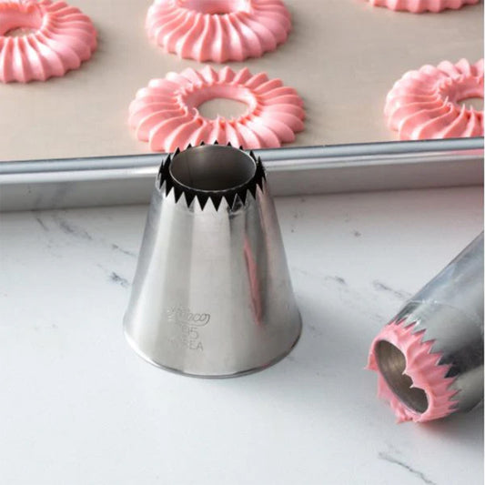 795 Sultan flat cone piping tip on a countertop near piped pink ruffled ring cookies on a baking sheet, with another metal tip in the foreground.