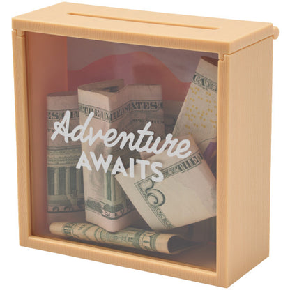 Adventure Awaits memory box cake topper with a transparent front and a slit on top, filled with folded dollar bills.