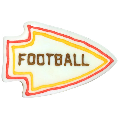 Decorated arrowhead-shaped cookie with white icing base, red and yellow piped border lines, and brown lettering across the center on a white background.