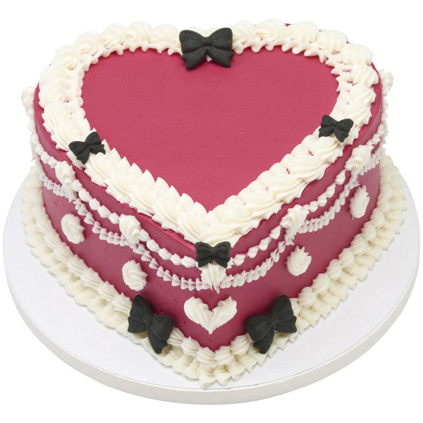 Heart-shaped cake with white frosting, red fondant, and black bow decorations on a white background
