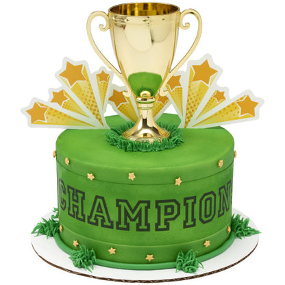 A green sports-themed cake with "CHAMPION" written on the side, topped with the gold trophy and starburst accents.