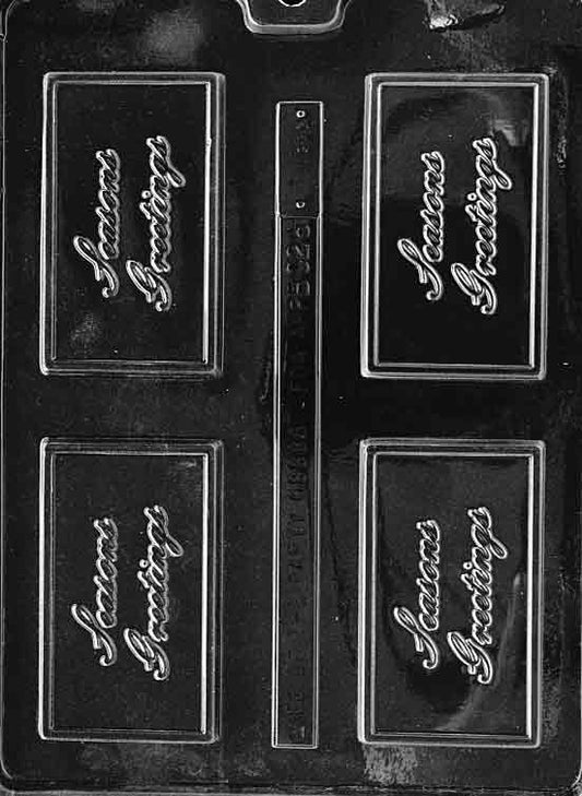 Clear chocolate mold in business-card size reading “SEASONS GREETINGS”; tidy rectangular border.
