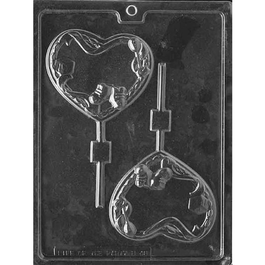 Clear plastic chocolate lollipop mold with two heart-shaped cavities, each decorated with raised baby-themed details including baby booties, blocks, and a rattle, shown on a dark background.