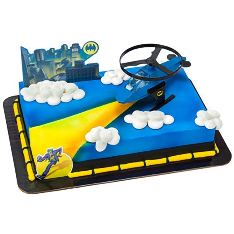 A rectangular cake decorated with a 'Batman' theme, featuring the Bat-Signal spotlight and a silhouette of Batman with the city of Gotham in the background, finished with a bold blue and yellow color scheme.