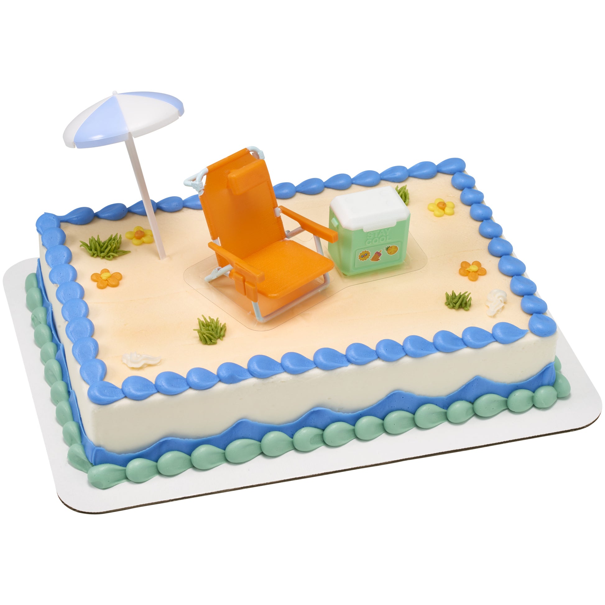 Beach chair and umbrella cake decorations placed on a frosted sheet cake with blue piping border and small flower accents, creating a beach scene.