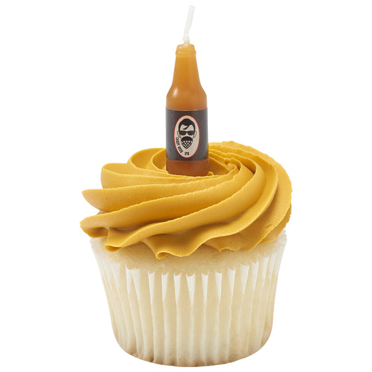 Miniature amber beer bottle birthday candle with black printed label and white wick displayed in a swirl of golden frosting on a cupcake.