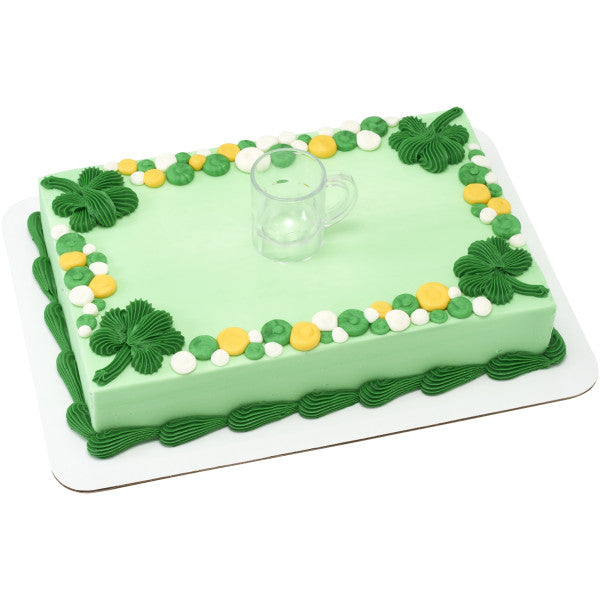 Rectangular sheet cake covered in pale green icing with piped green corner swirls and a border of green, yellow, and white dots, topped at center with a small clear beer mug layon.