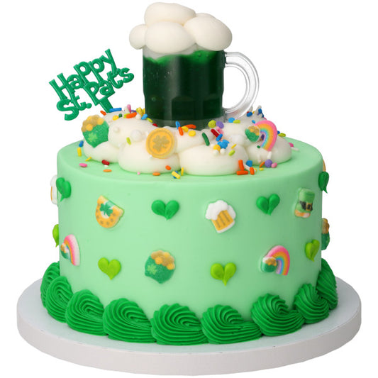 St. Patrick’s Day themed cake with mint green frosting, green ruffle border, shamrock decorations, and a beer mug topper filled with dark green “beer” and white foam on top.