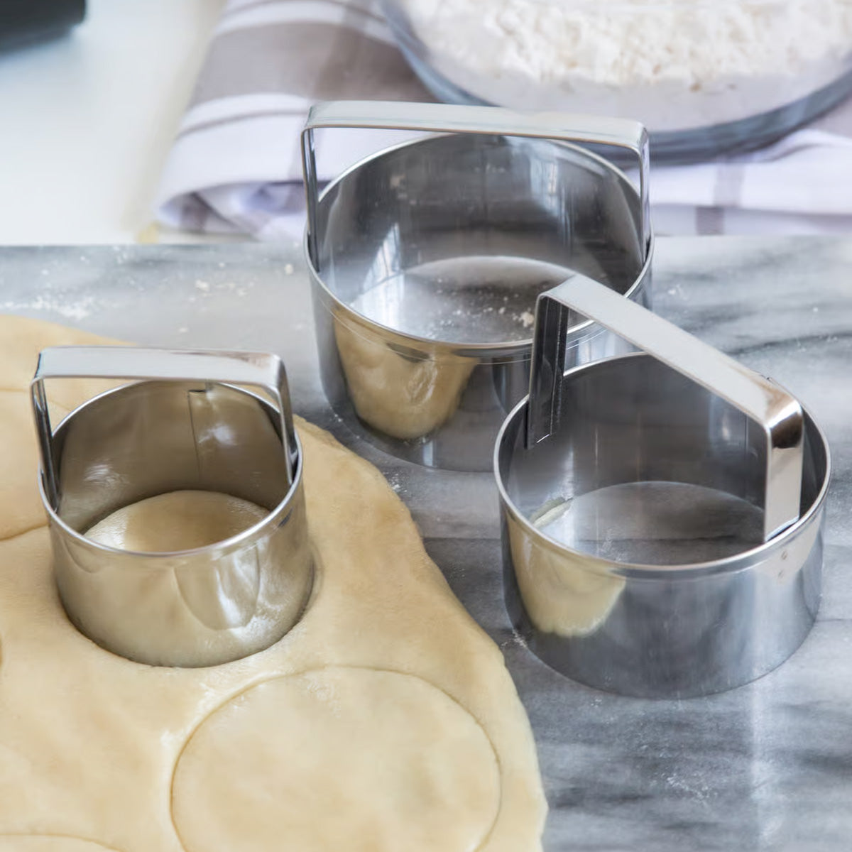 Biscuit cutters cutting circular shapes from dough on a marble countertop.