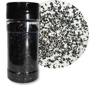 Clear shaker jar filled with black edible glitter flakes beside a white circular surface scattered with irregular black sparkling pieces.